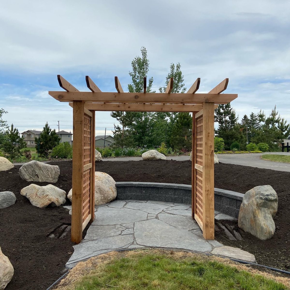 Cedar arbor with lattice panels over a flagstone circle, boulders set around it
