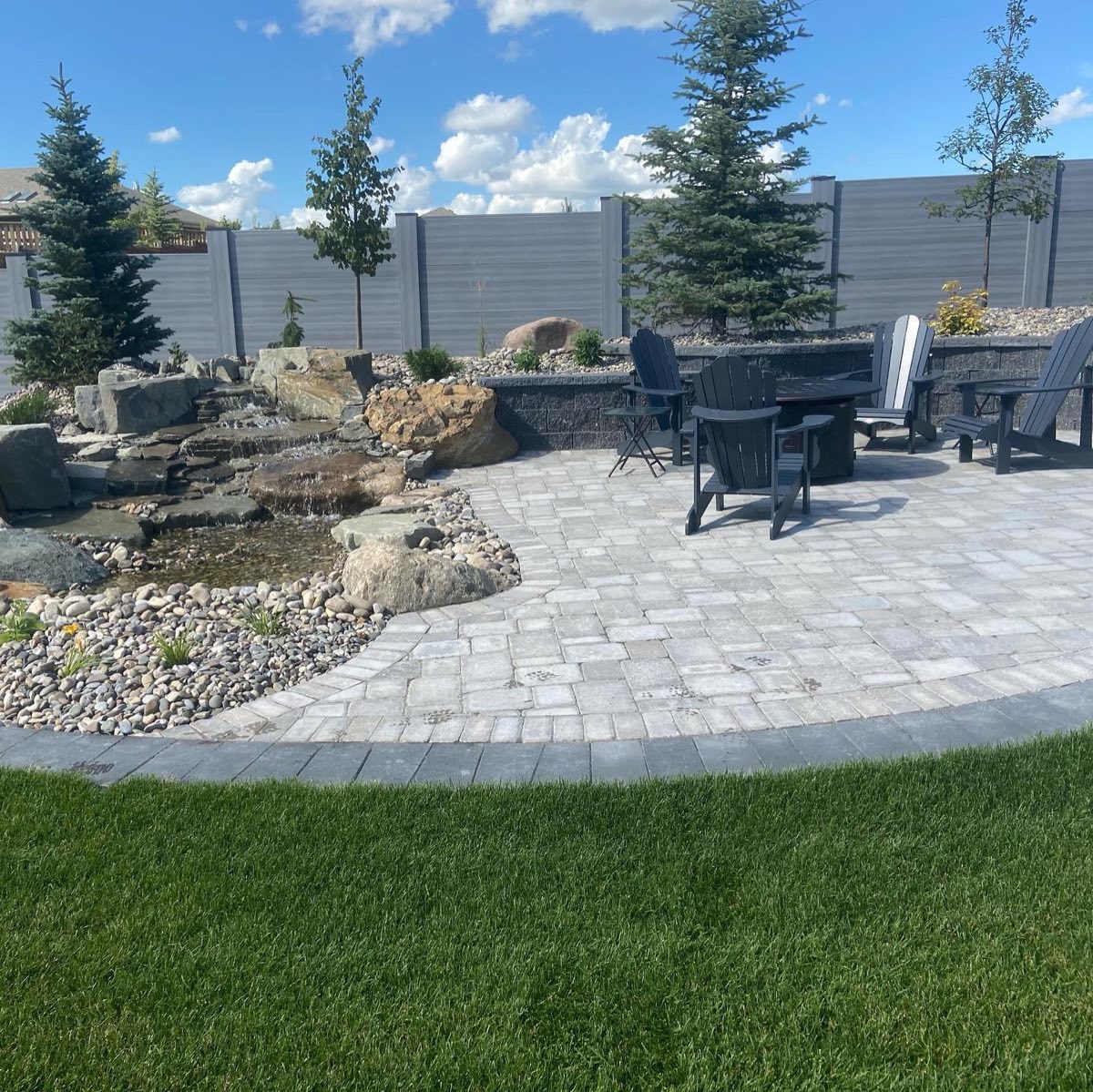 Backyard waterfall beside a paver patio with chairs around a fire table