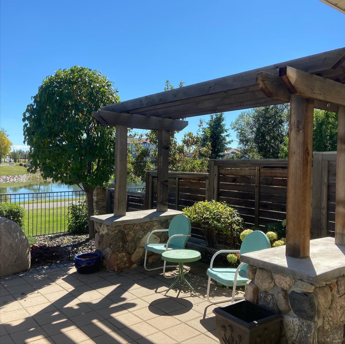 Pergola over a stone-pillared patio overlooking a pond